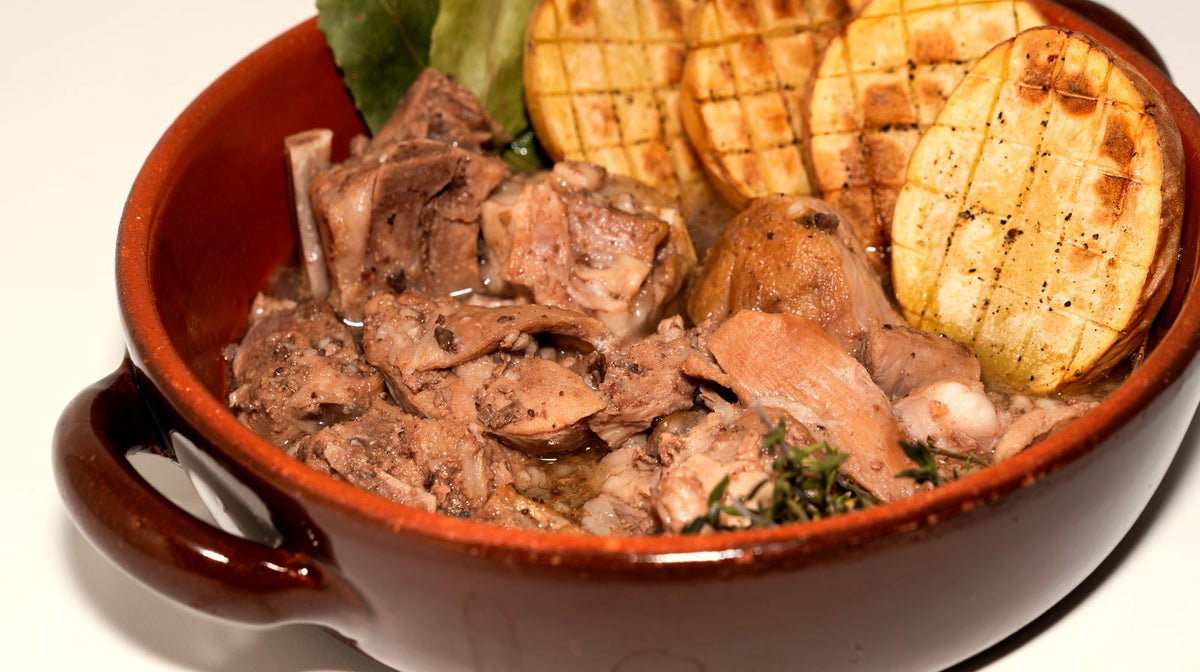 Cabrito confitado servido en cazuela de barro con patatas asadas, laurel y tomillo