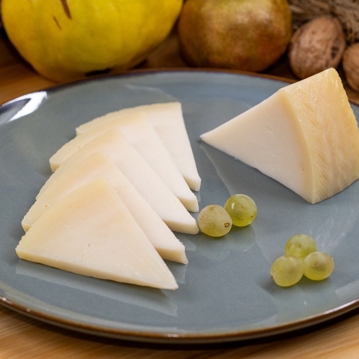 Cuñas de queso de cabra curado ecológico en plato azul con uvas